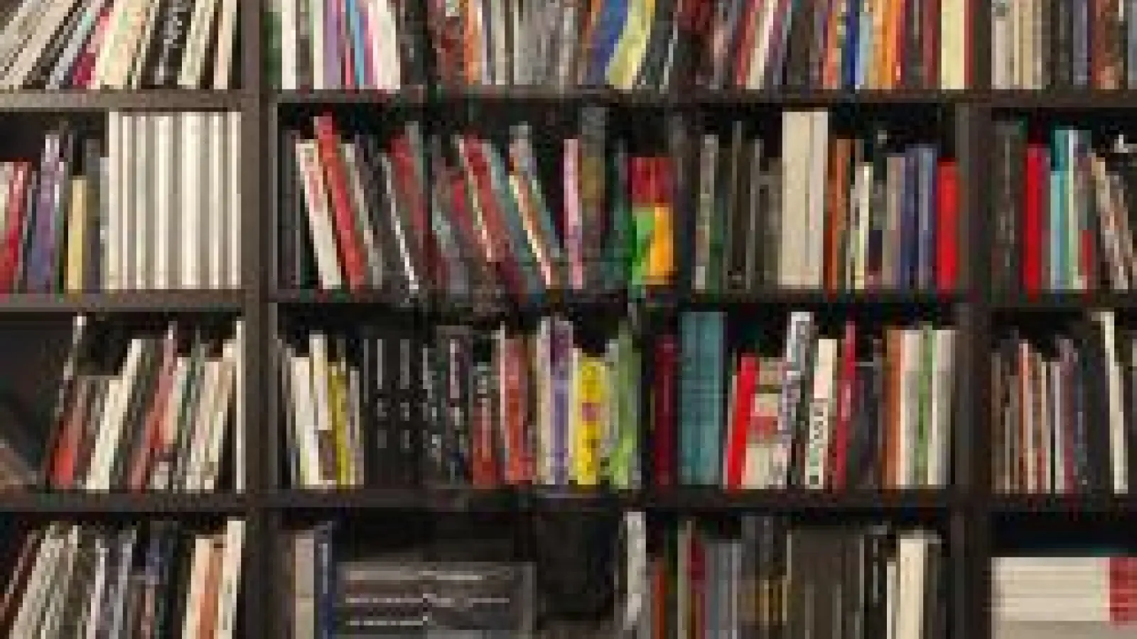 A wall of bookshelves, crowded with books both upright and lying on their sides