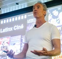 Frederick Luis Aldama speaks in front of a large screen displaying Latinx movie posters